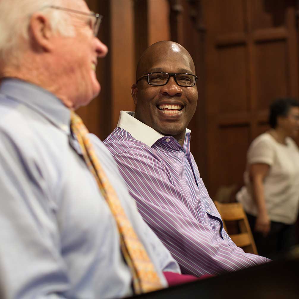 Two men laugh together during choir practice.