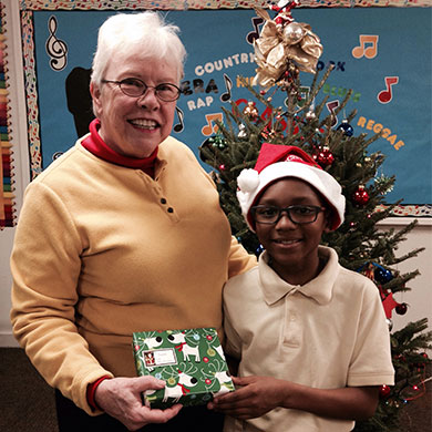 A Brown member and volunteer tutor stands with a student and his Christmas present.