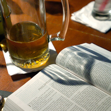 Image of glass of beer next to an open Bible.