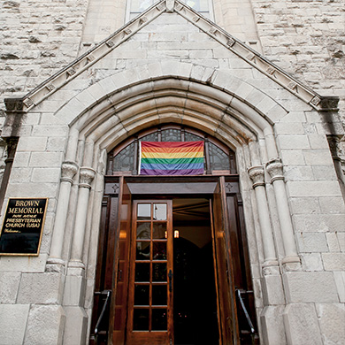 A photo of Brown's front door standing open, with the rainbow flag above it.