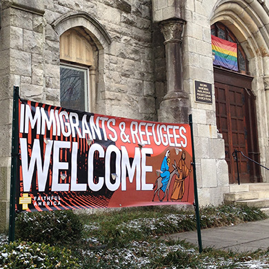 A banner is displayed outside Brown Memorial that says "Immigrants & Refugees Welcome."