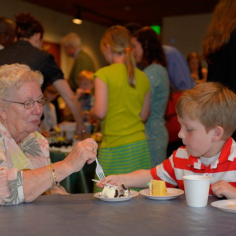 A boy and his grandmother enjoy a piece of cake during a community potluck after Sunday worship.