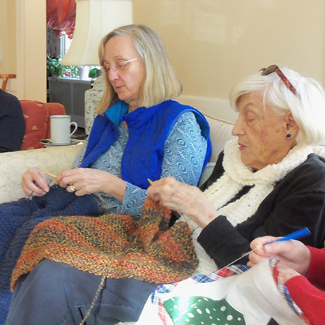 Women sit on couches in a church member's home and knit shawls.