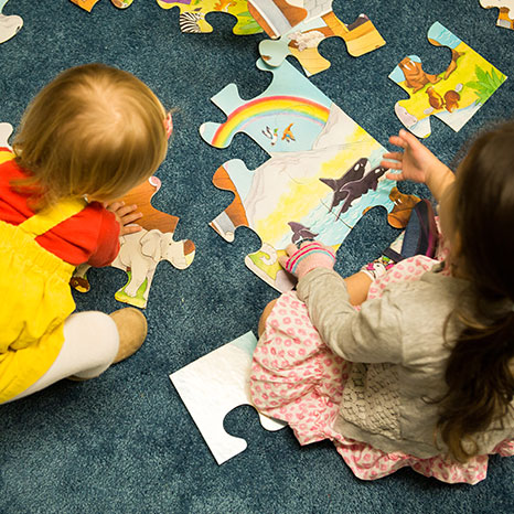 Two children sit on the floor in the Nursery and put a puzzle together.
