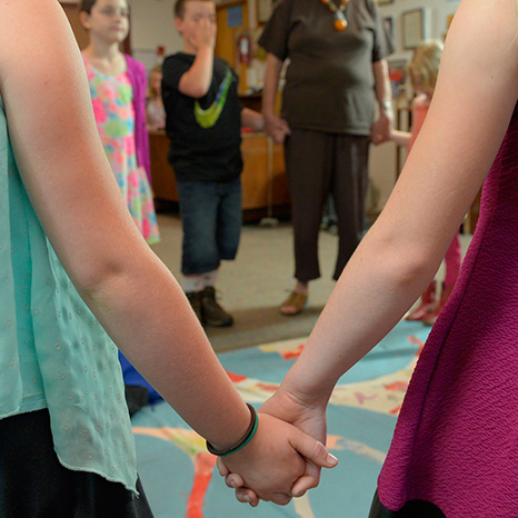 Two girls hold hands while the Sunday morning Bible study class stands in a circle and says a prayer.