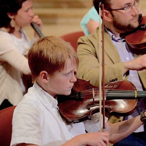 A young boy plays the violin with the Brown Memorial instrumental ensemble during worship.