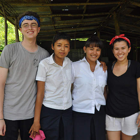 Youth from Brown Memorial visit a school in El Salvador and stand with two girls to smile for the photo.