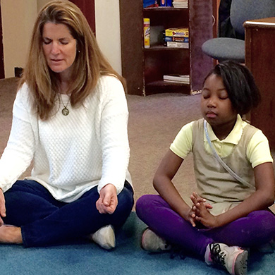 A student and a Tutoring staff member sit with their eyes closed, meditating.
