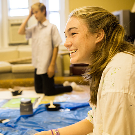 A girl smiles while painting a canvas during a Sunday morning class at Brown.