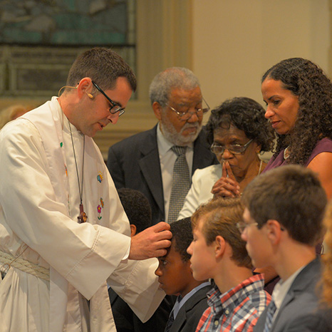 Andrew Foster Connors blesses a youth kneeling while being confirmed.