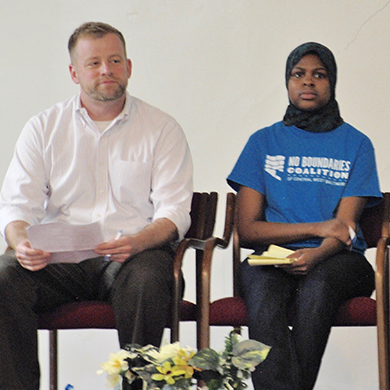 Rev. Tim Hughes Williams sits on a stage with BYOP leader Samirah Franklin at a meeting with the Mayor.