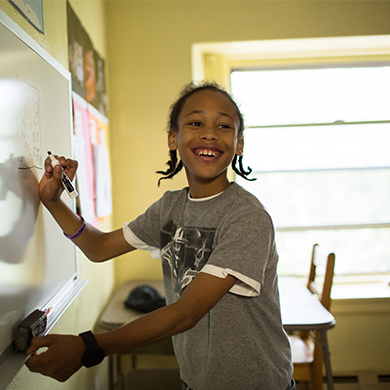 A Brown Memorial Tutoring Program students smiles as he writes on a dry erase board in a classroom at Brown Memorial.