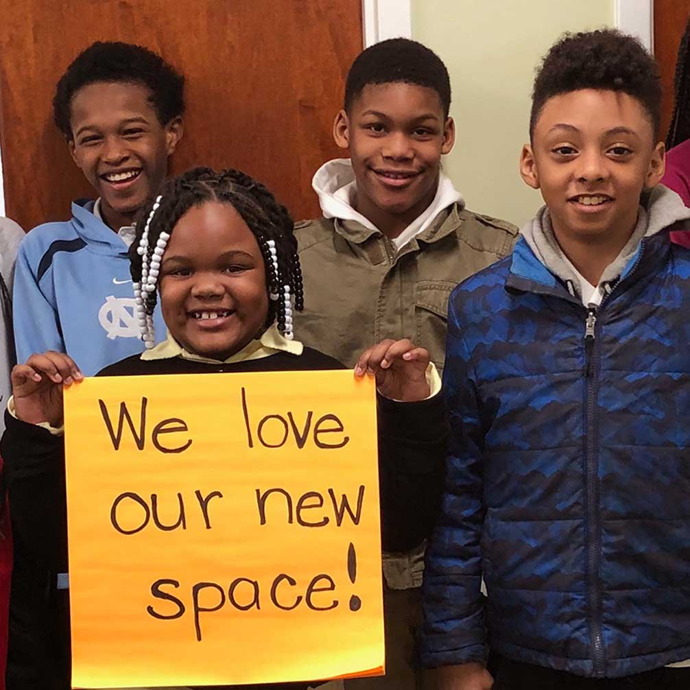 Students in the Brown Memorial Tutoring Program hold up a sign that says, "We love our new space!"