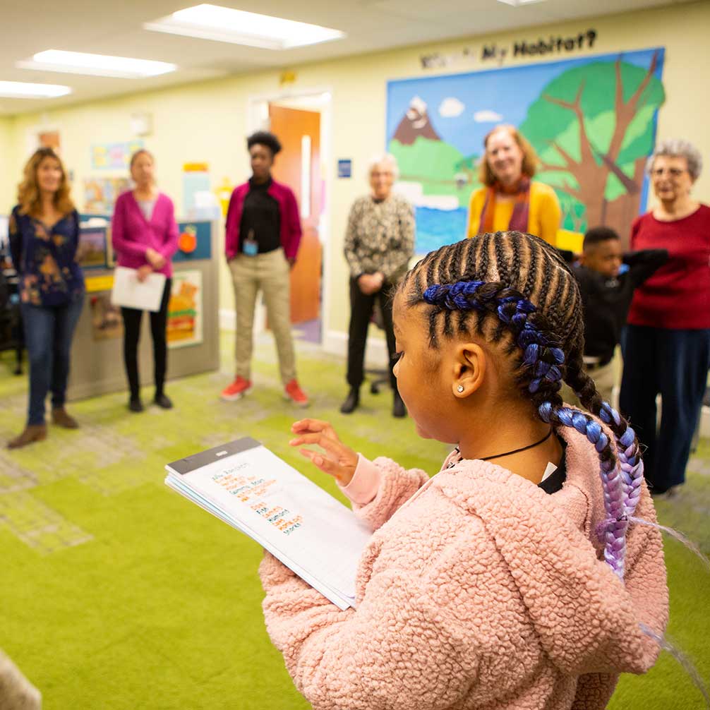 A girl reads to the tutors gathered in a circle during a session at the Brown Tutoring Program.