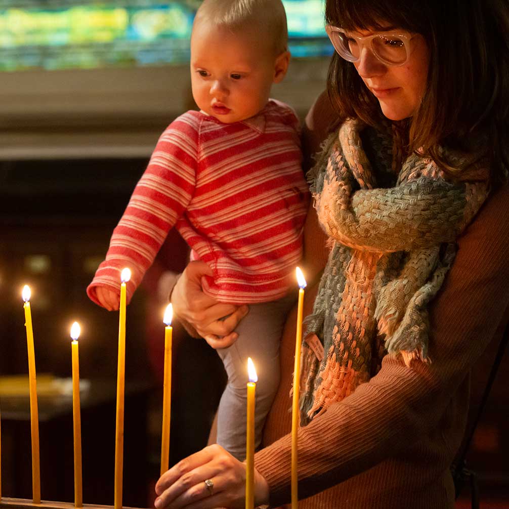 A woman lights a candle during worship while holding her daughter.