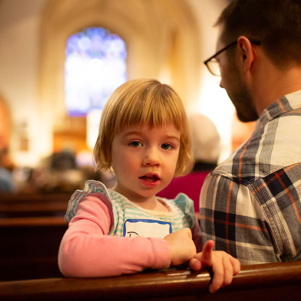 A little girl looks over the edge of the pew during worship.