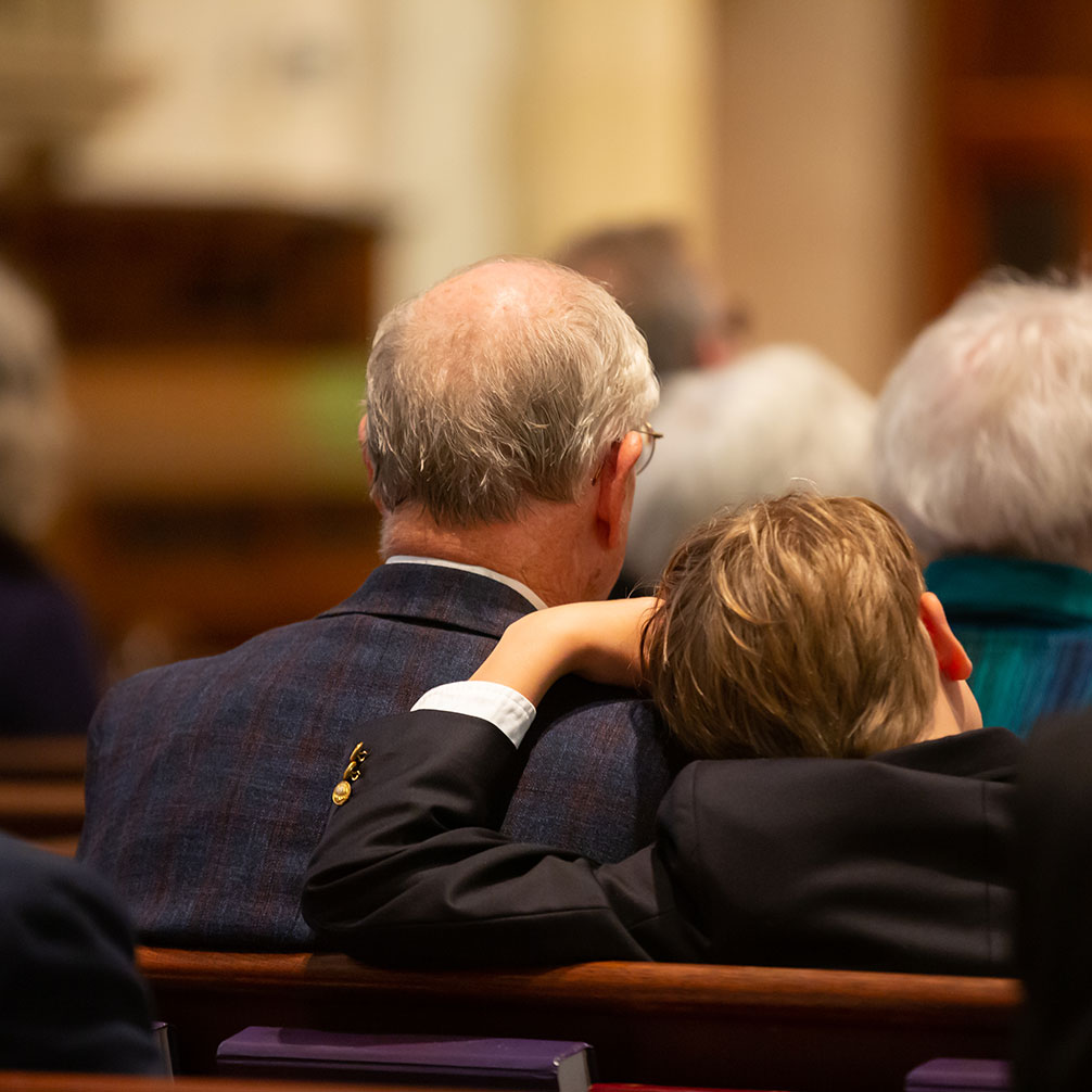 A boy rests his head on his grandfather's shoulder during worship.