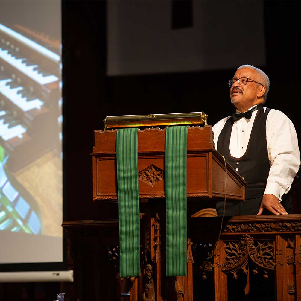 An organist speaks at the lecturn during a Tiffany Series concert.