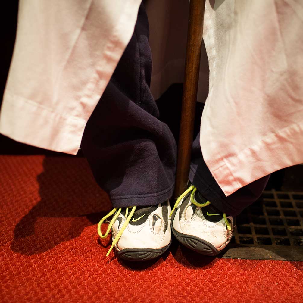 A child sits with his tennis shoes peeking out from under his alter robe.